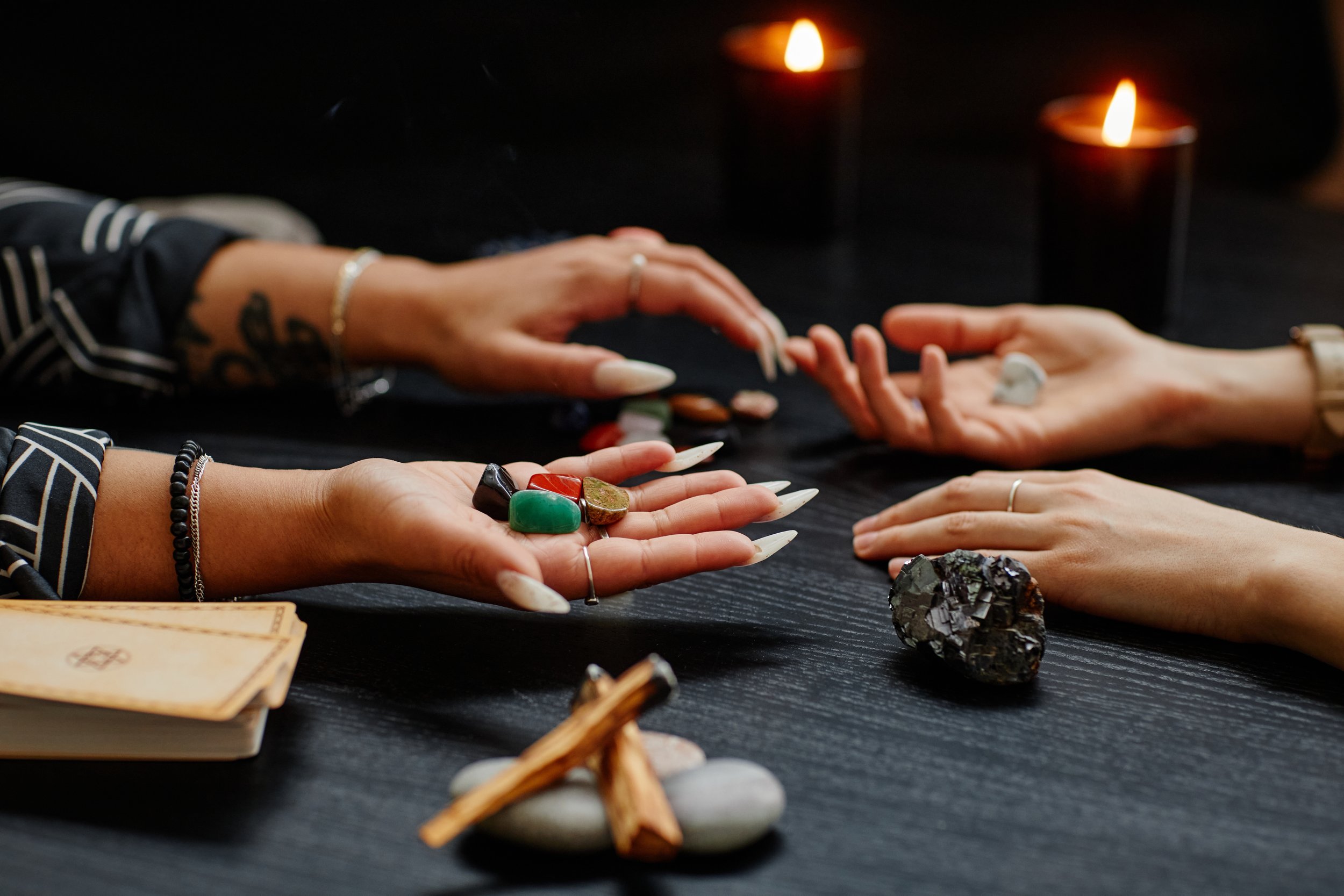 woman with long nails extending hand with crystals in her palm with crystal and stack of cards in foreground on table