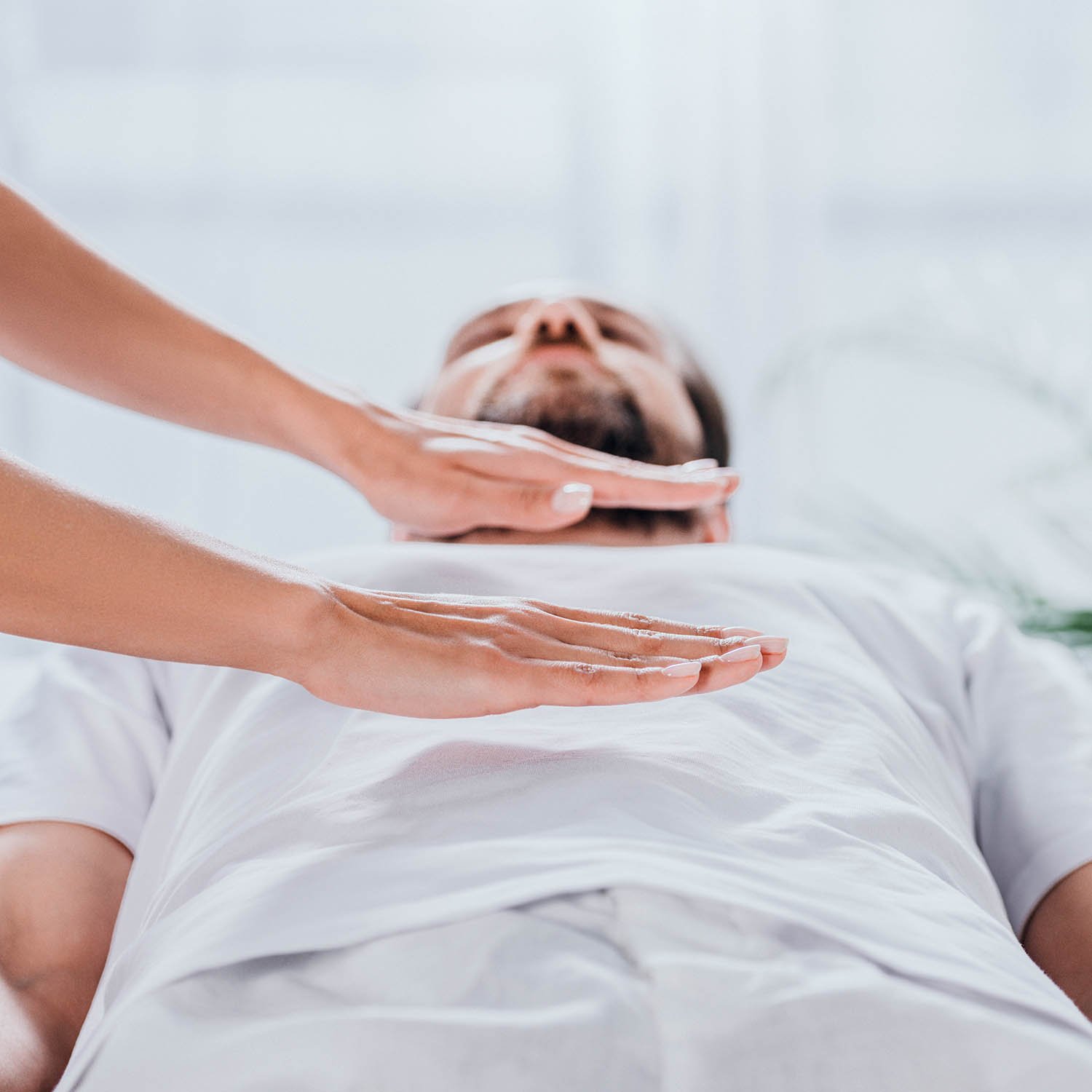 Reiki energy healer's hands positioned over the central line of a man's body. The man in a white shirt is receiving the healing.
