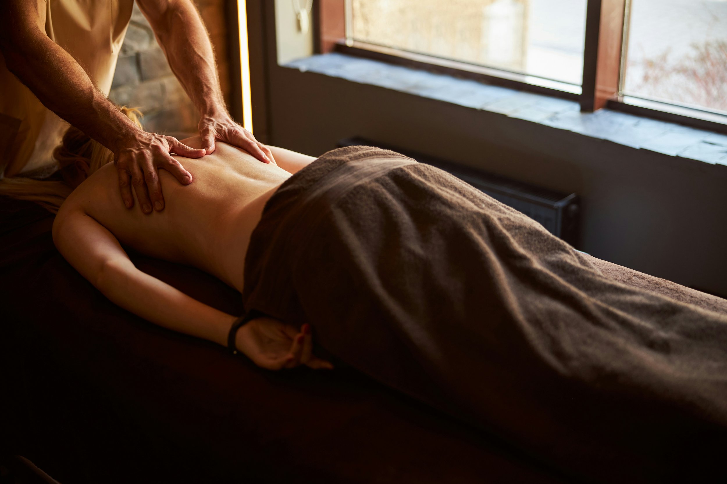 massage therapist with hands on the upper back of a woman receiving a massage on table